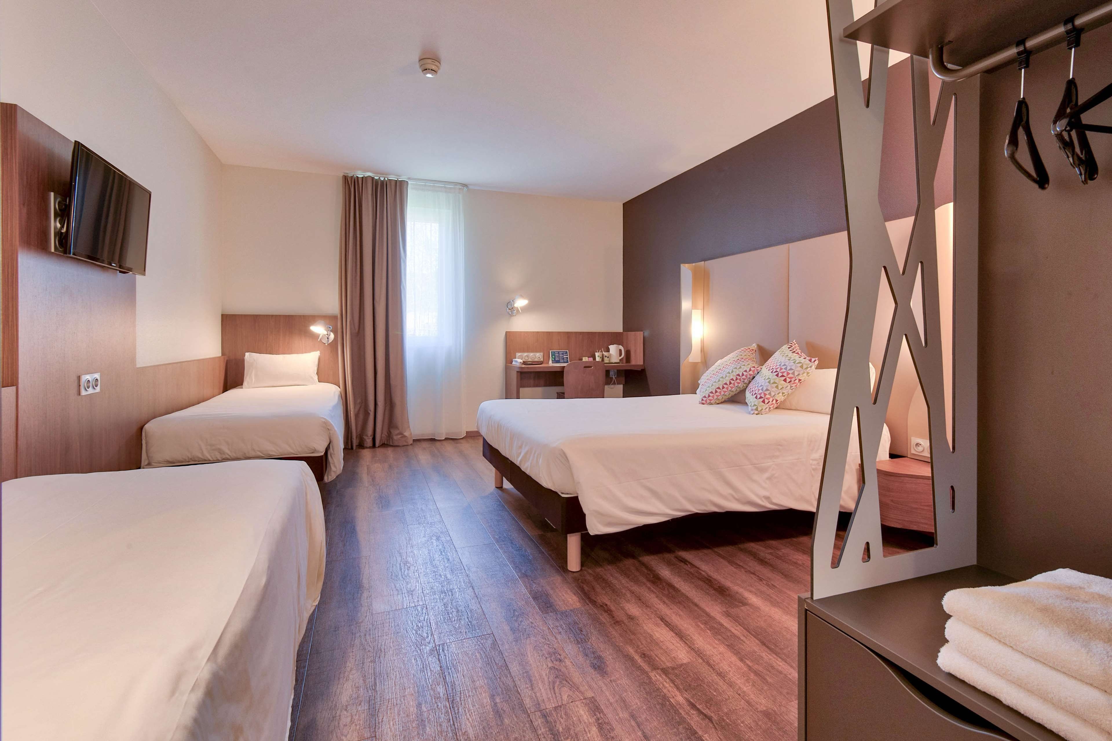 Habitación de hotel con dos camas, un televisor, un escritorio y un espejo de baño.