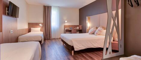 Habitación de hotel con dos camas individuales, un escritorio con silla, un televisor montado en la pared y una ventana con cortinas.