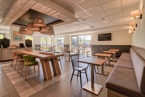 A spacious restaurant with wooden tables and chairs, a long counter, and a seating area with a bench. - Campanile PRIME - Saint Jean de Luz (Saint-Jean-de-Luz)
