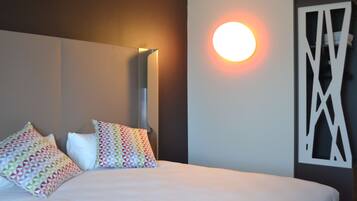 Une chambre d’hôtel comprenant un lit, deux oreillers, une lampe fixée au mur et un panneau décoratif.