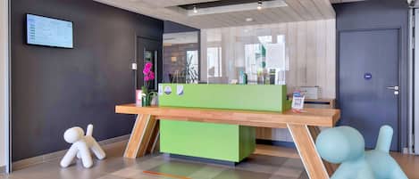 Una recepción con un mostrador verde, piso de madera y una puerta con un cartel azul.