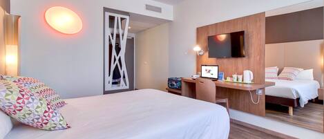 A modern hotel room with a large bed, a desk with a computer, a TV, and a mirror.