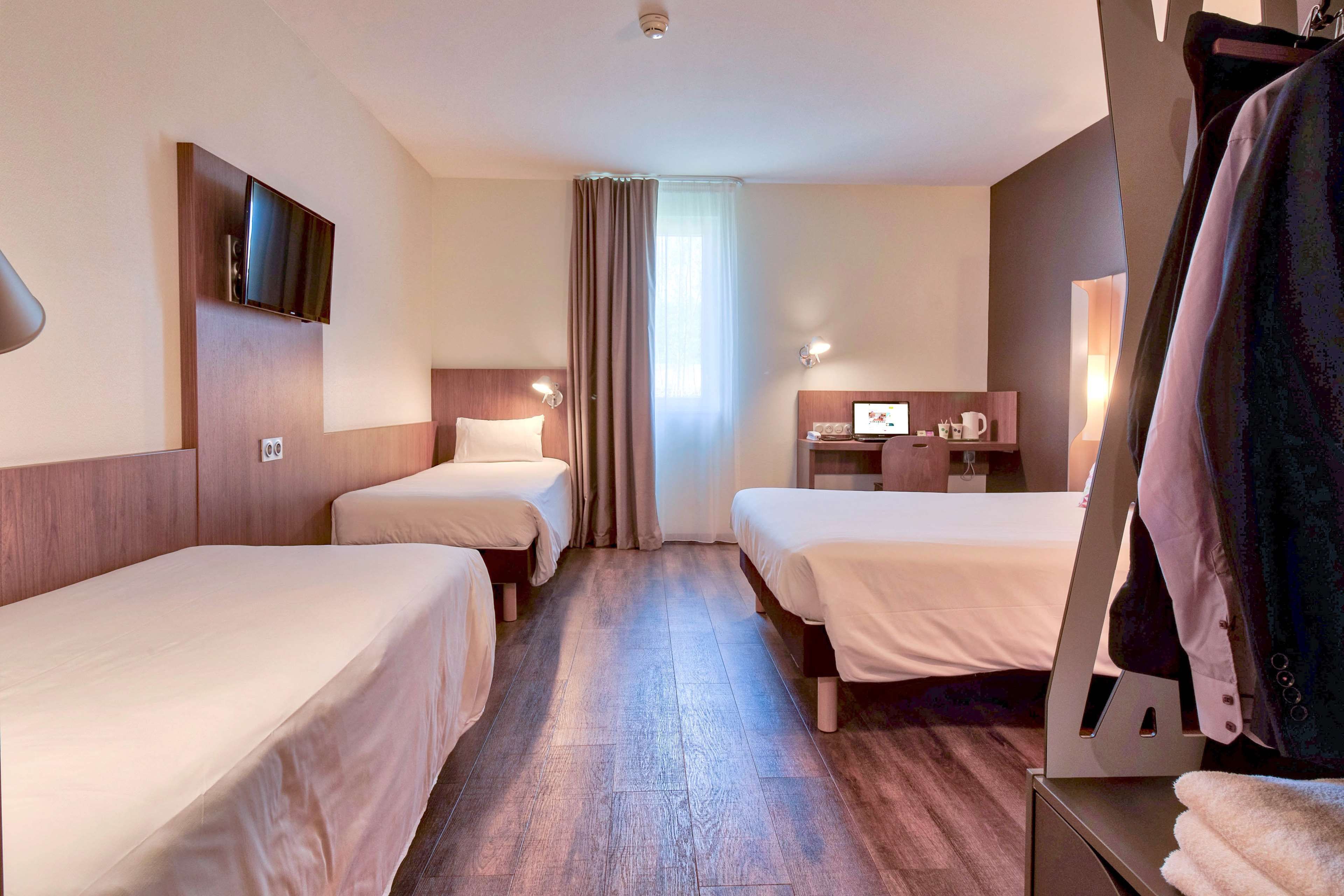 A hotel room with two single beds, a desk with a computer, a TV mounted on the wall, and a wardrobe.