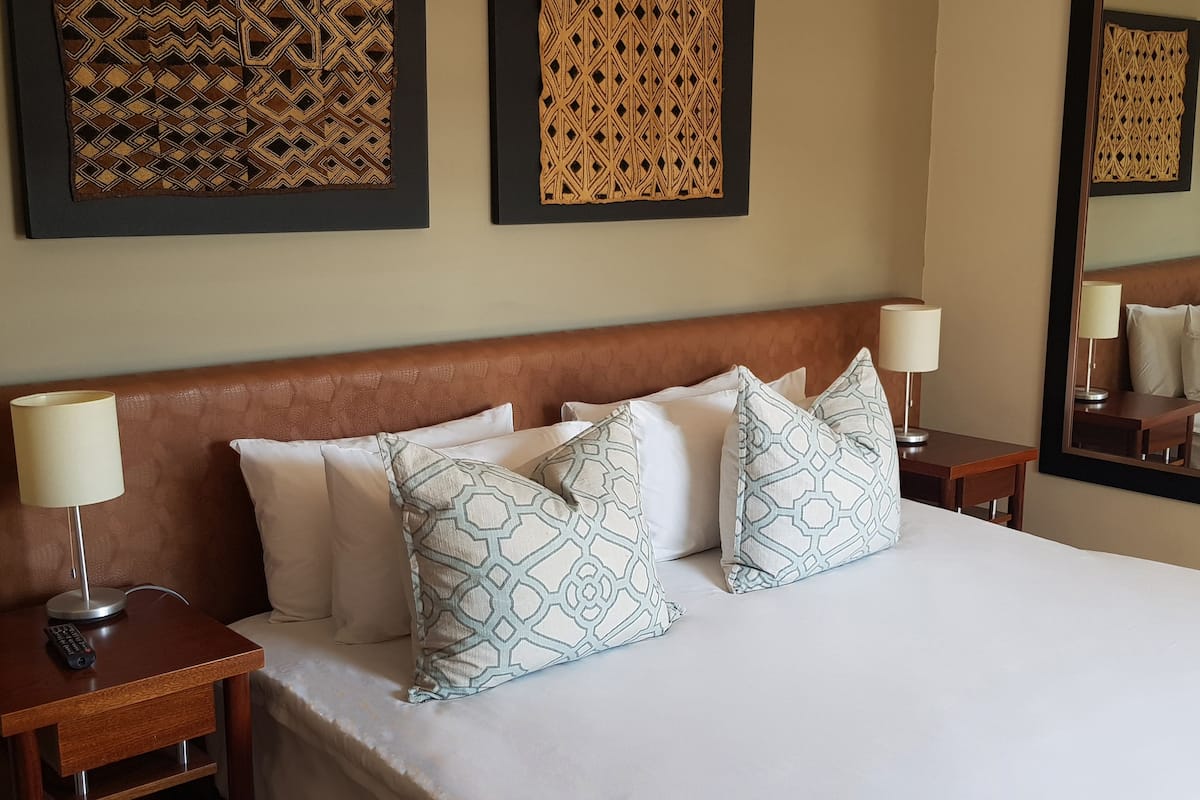 A hotel room with a large bed, multiple pillows, two bedside tables with lamps, and two wall-mounted decorative panels.