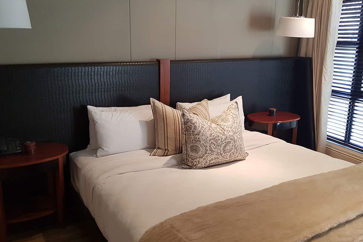 A hotel room with a large bed, two bedside tables, a lamp, and a window with blinds.