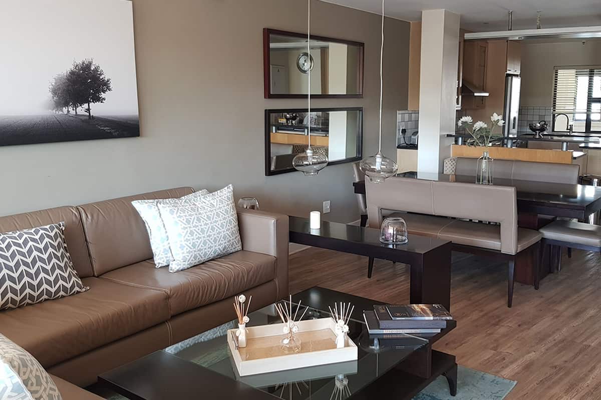 A modern living room with a brown leather sofa, a glass coffee table, and a dining area with a bench and table.
