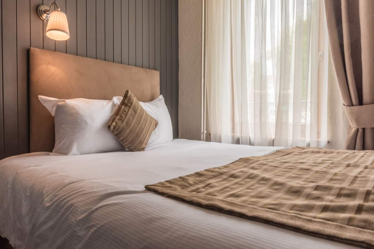 A neatly made bed with a headboard, a bedside lamp, and sheer curtains.