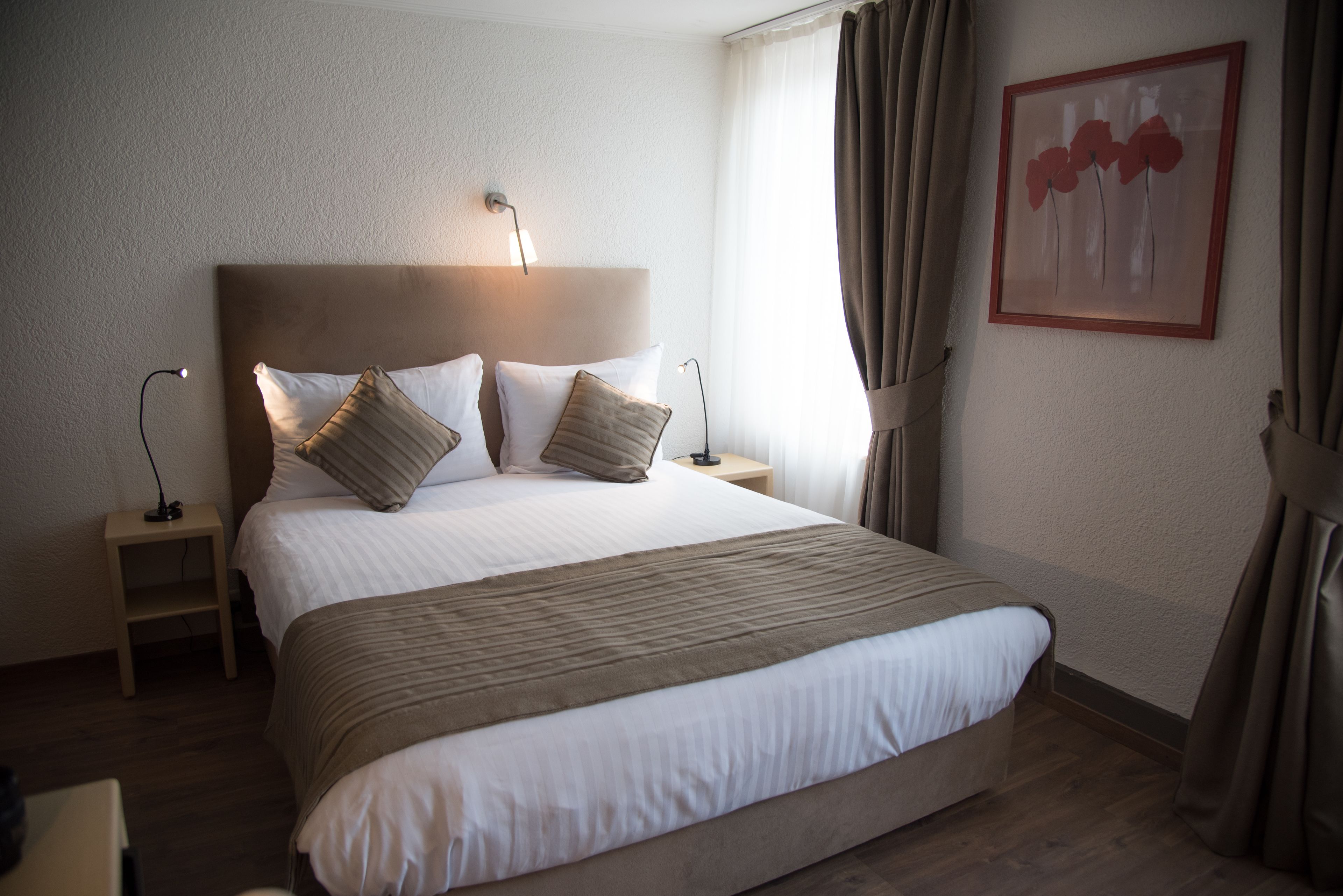 Habitación de hotel con una cama grande, dos mesitas de noche, una lámpara de pared y una obra de arte enmarcada.