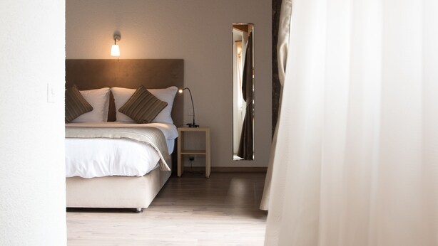 A bedroom with a wooden ceiling, a bed with white bedding, a nightstand, and a mirror. - Hôtel de l'Ange (Nyon)