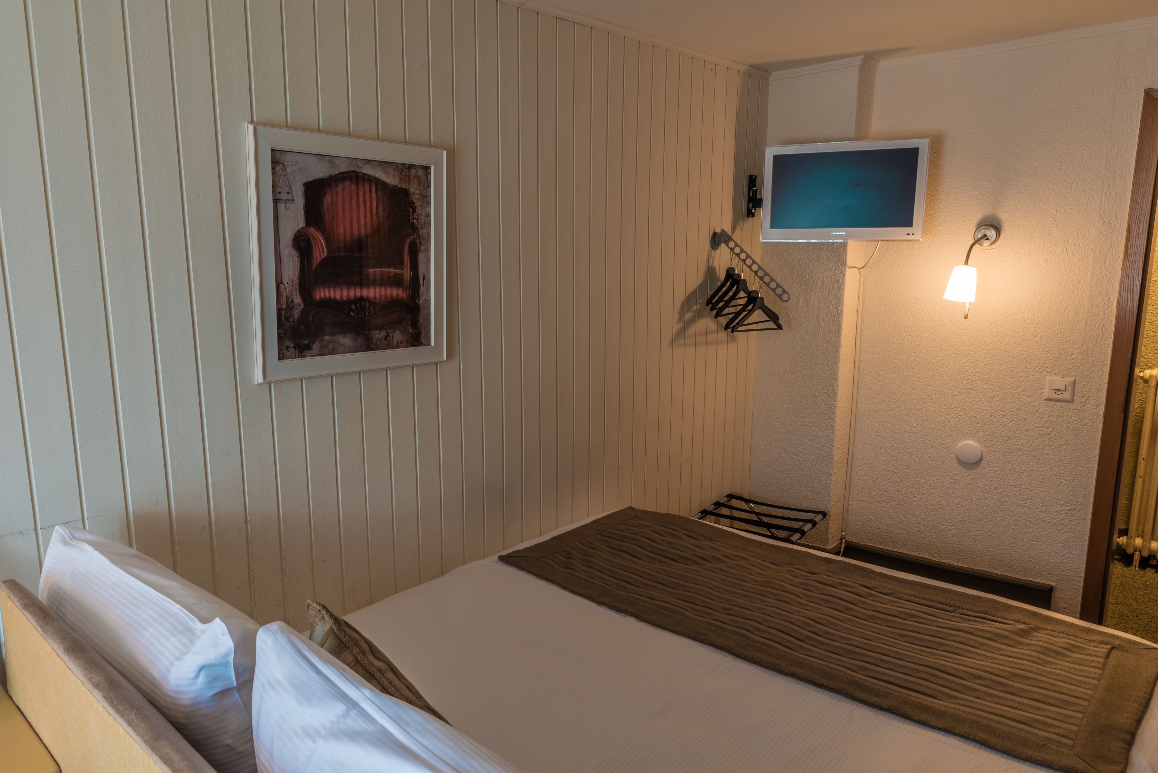 A room with a bed, a television mounted on the wall, and a framed picture above the bed.