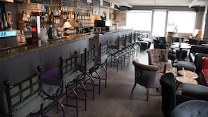A bar area with a long counter, multiple chairs, and a variety of bottles and glasses. - Hôtel de l'Ange (Nyon)