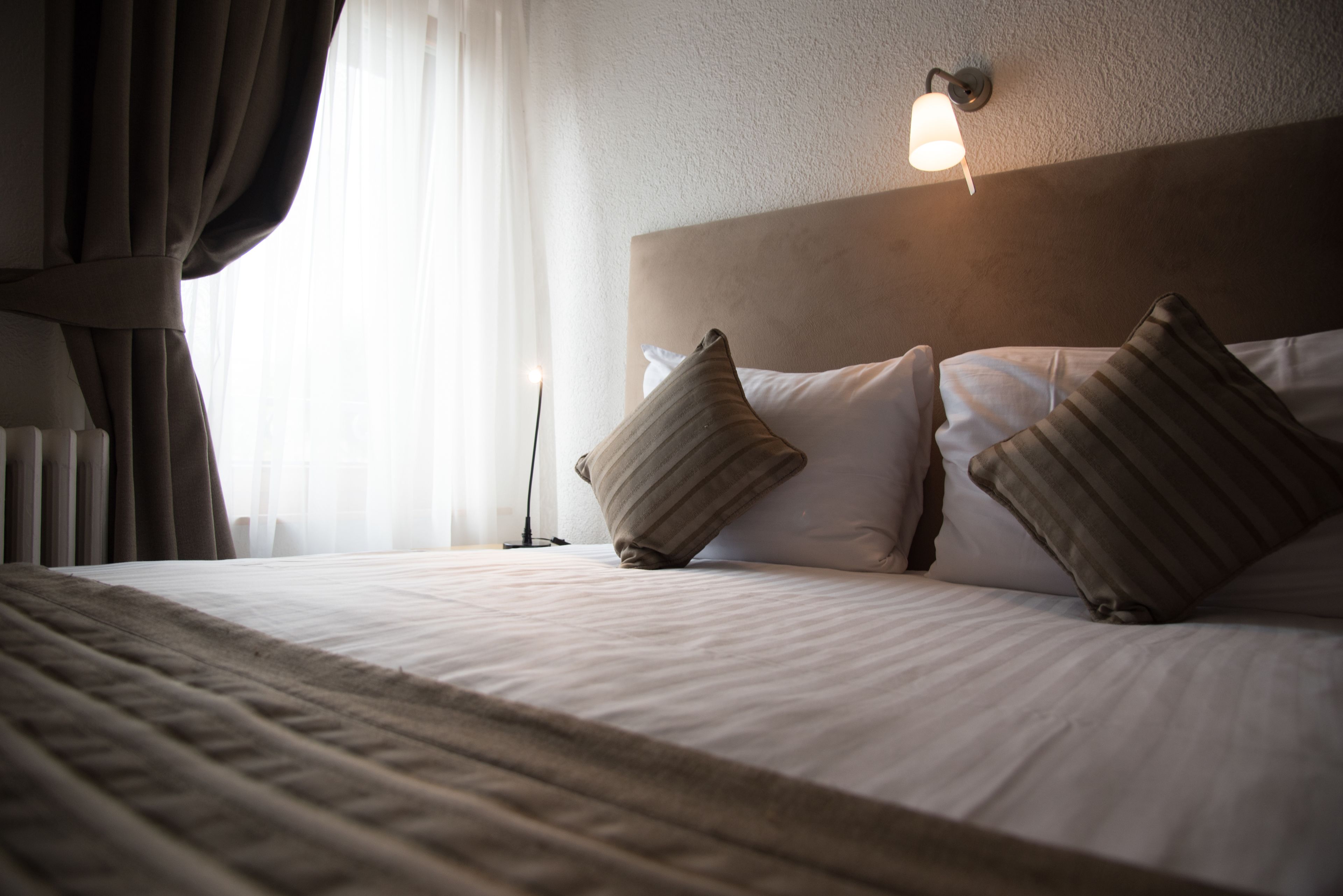 A neatly made bed with a headboard, two pillows, and a bedside lamp.