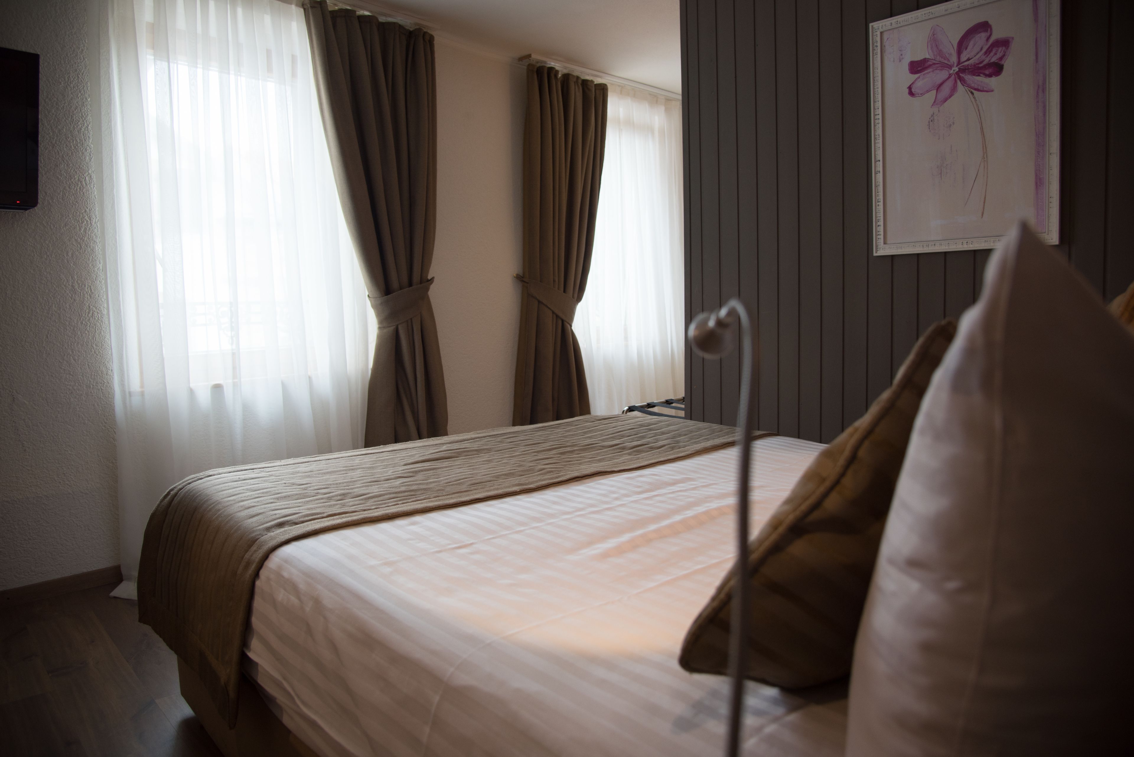 A neatly made bed with a headboard, a bedside lamp, and a framed artwork on the wall.