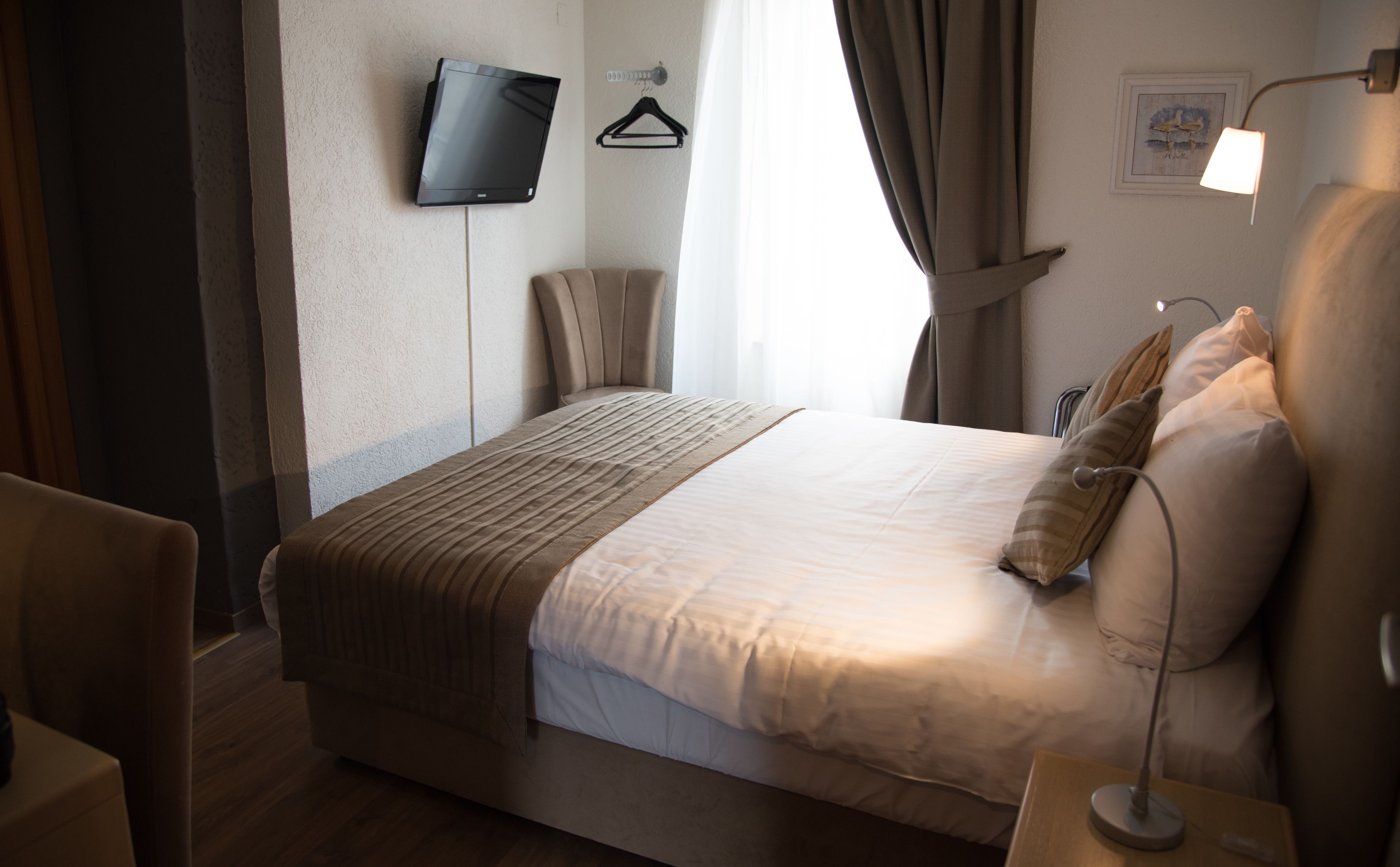 A neatly made bed with a striped blanket, a bedside table with a lamp, a television mounted on the wall, and a framed picture on the wall.