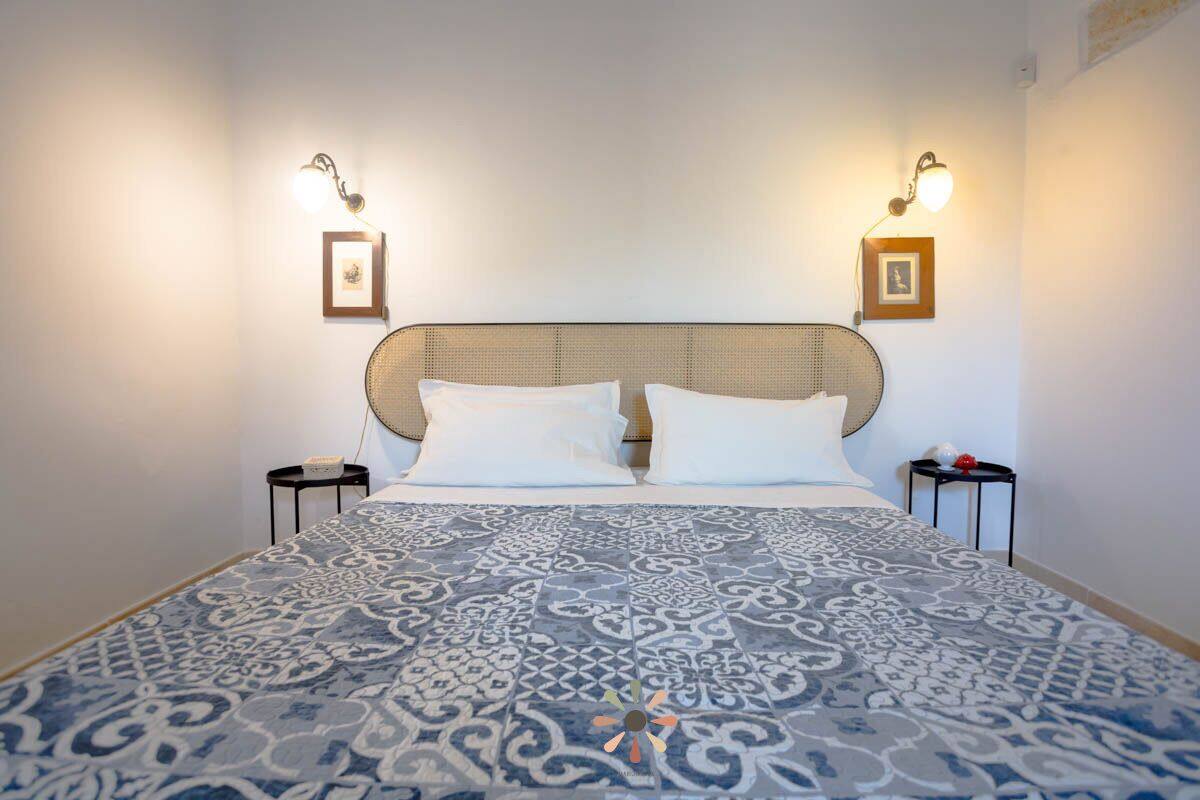 A neatly made bed with a patterned bedspread, two bedside tables with lamps, and framed pictures on the walls.