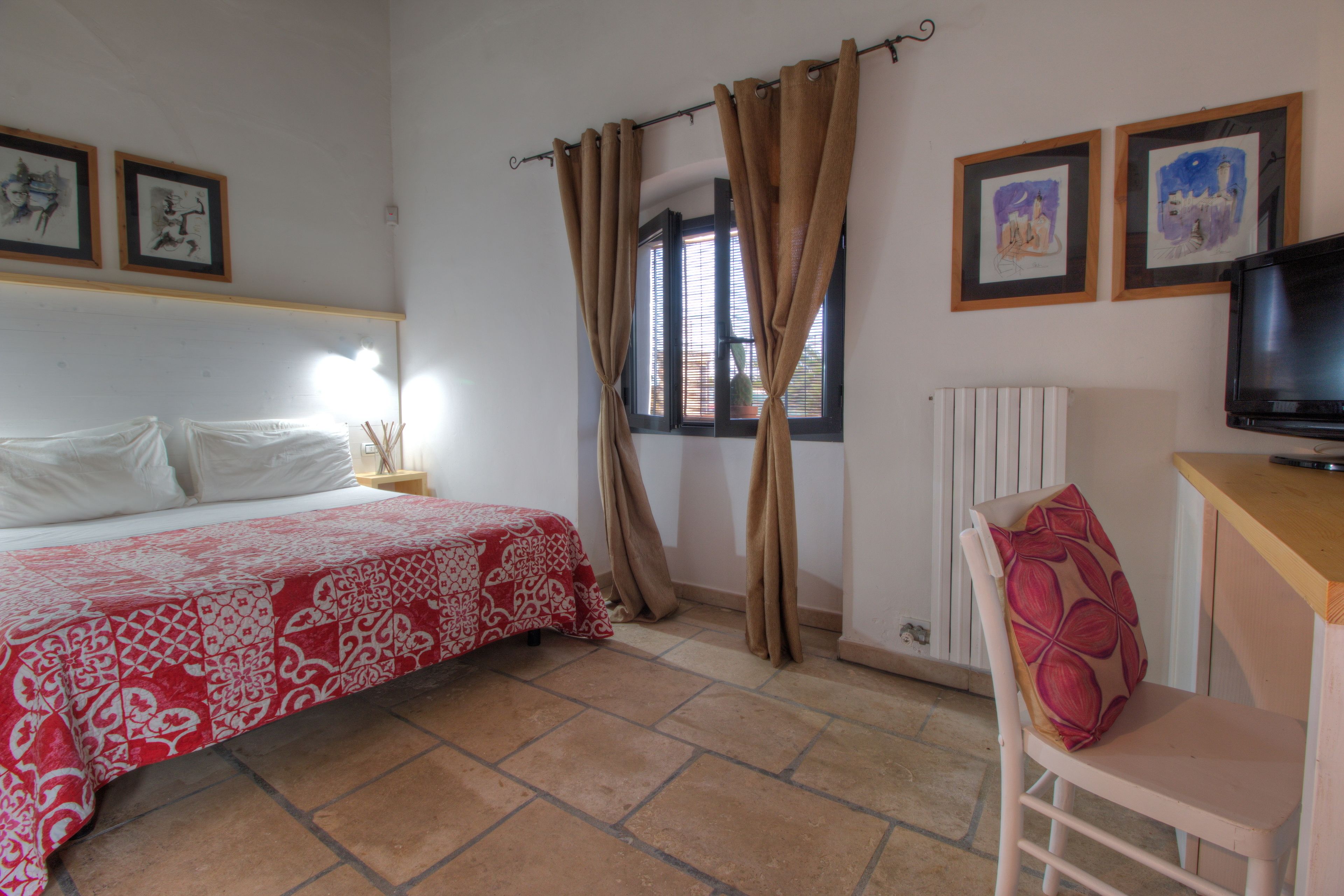 Un dormitorio con cama, una silla, televisión y obras de arte en la pared.
