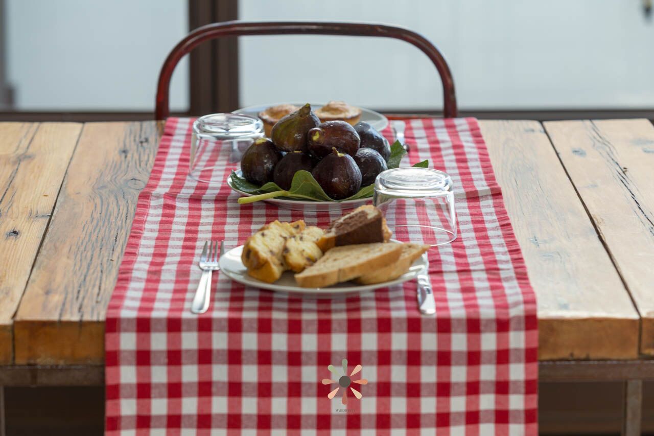 A wooden table with a red and white checkered tablecloth, a plate with bread and figs, and a glass jar.