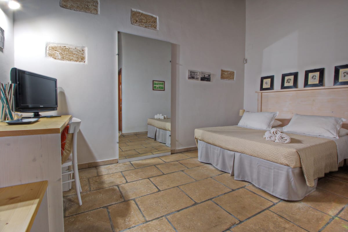 A bedroom with a bed, a desk with a computer, and a mirror.