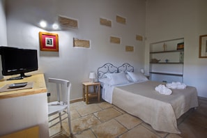 A hotel room with a bed, a desk with a computer, a chair, and a small table with a lamp.
