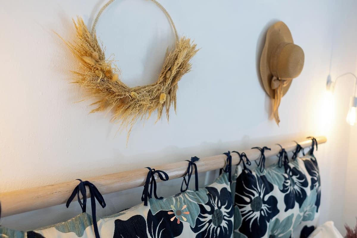 A wall with a decorative wreath, a hat, and a curtain rod with floral curtains.