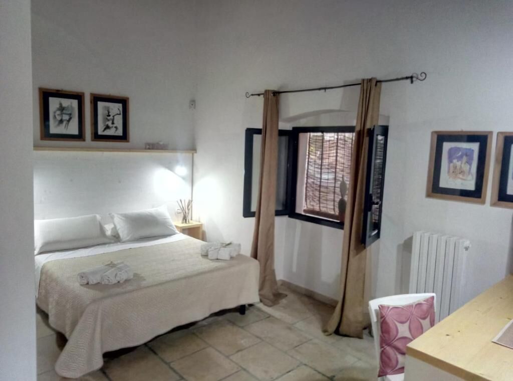 A bedroom with a bed, a window with curtains, a radiator, and framed pictures on the wall.