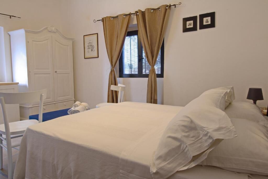 A bedroom with a bed, a chair, a desk, and a window with curtains.