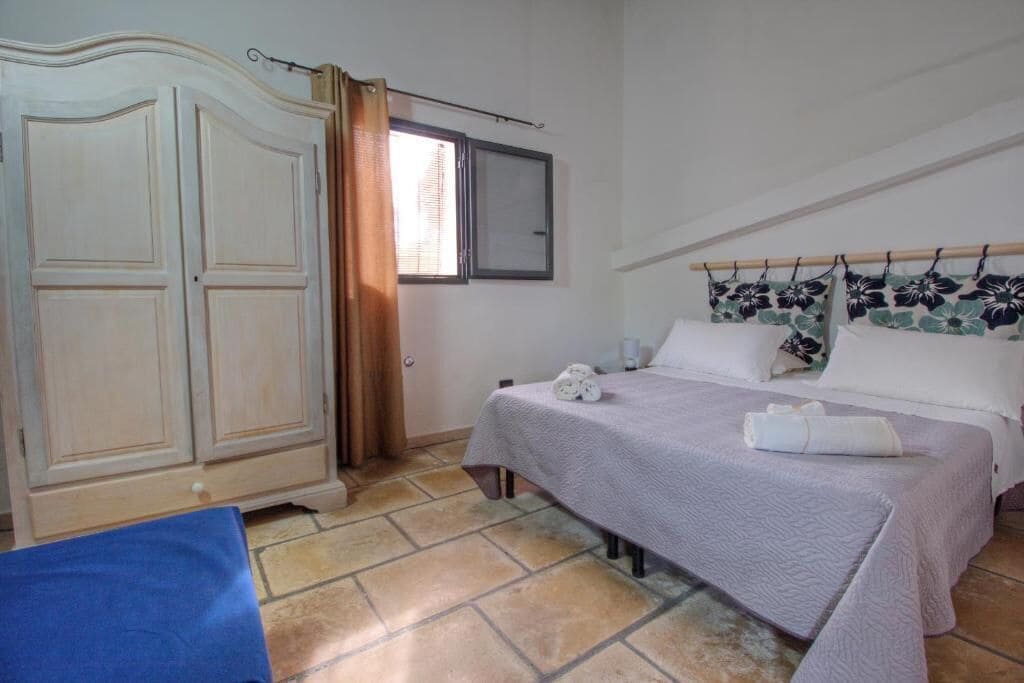 Une chambre à coucher avec un lit, une armoire, une fenêtre avec des rideaux et une petite table.