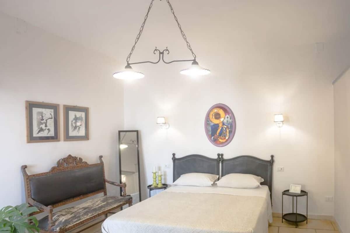 A bedroom with a bed, a bench, a mirror, and wall art.