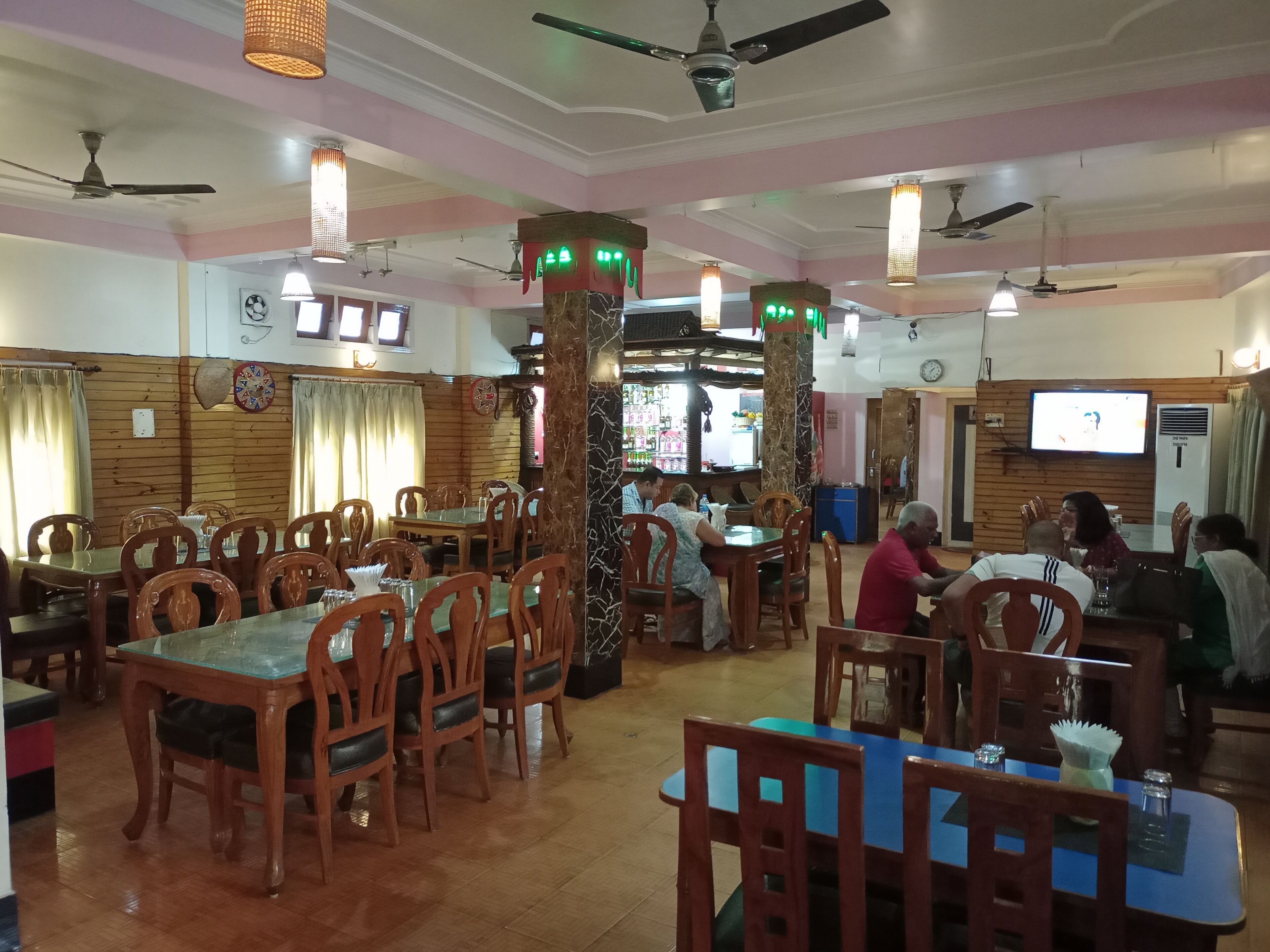 A restaurant with wooden walls, multiple tables and chairs, ceiling fans, and a television screen.