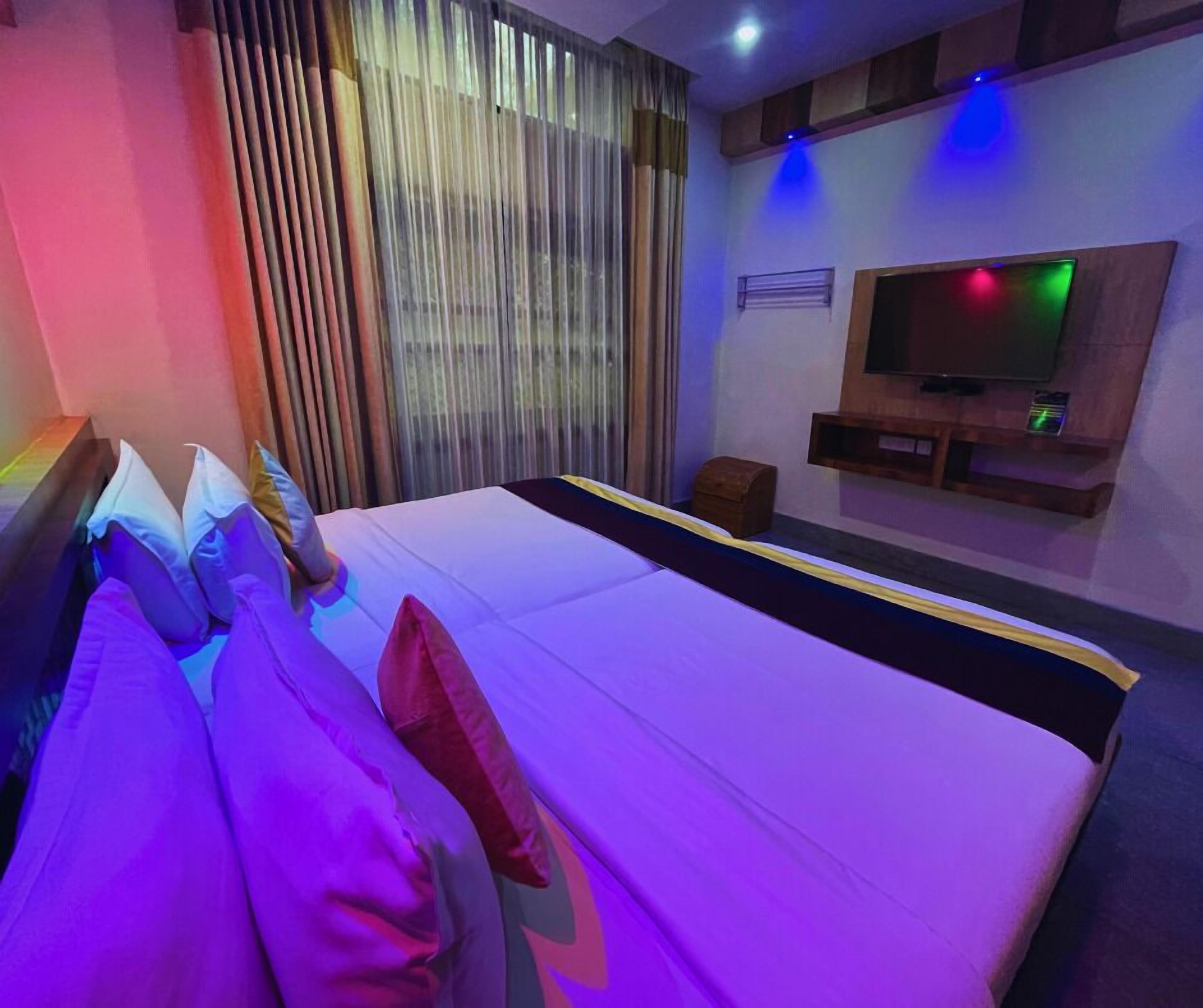 A hotel room with a bed, pillows, a TV, and a small wooden chest.