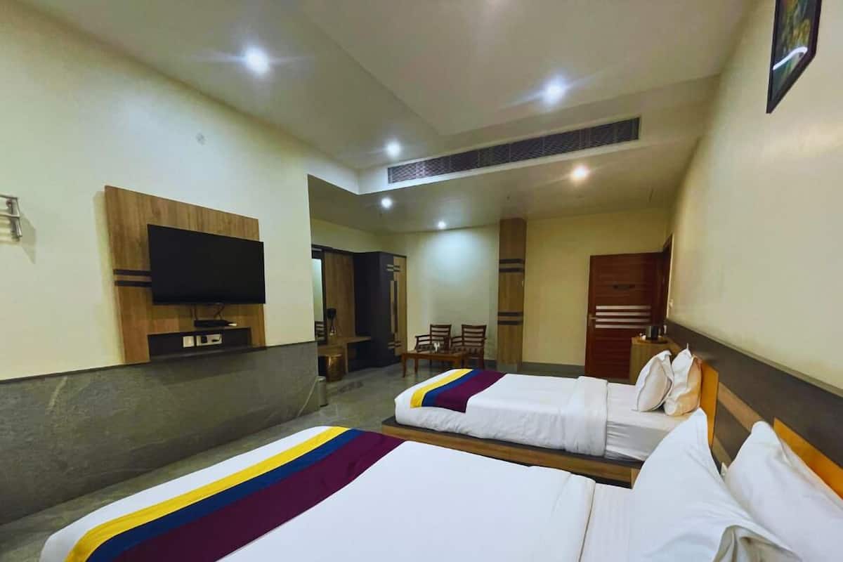 A hotel room with two beds, a TV mounted on the wall, and a small seating area with chairs.
