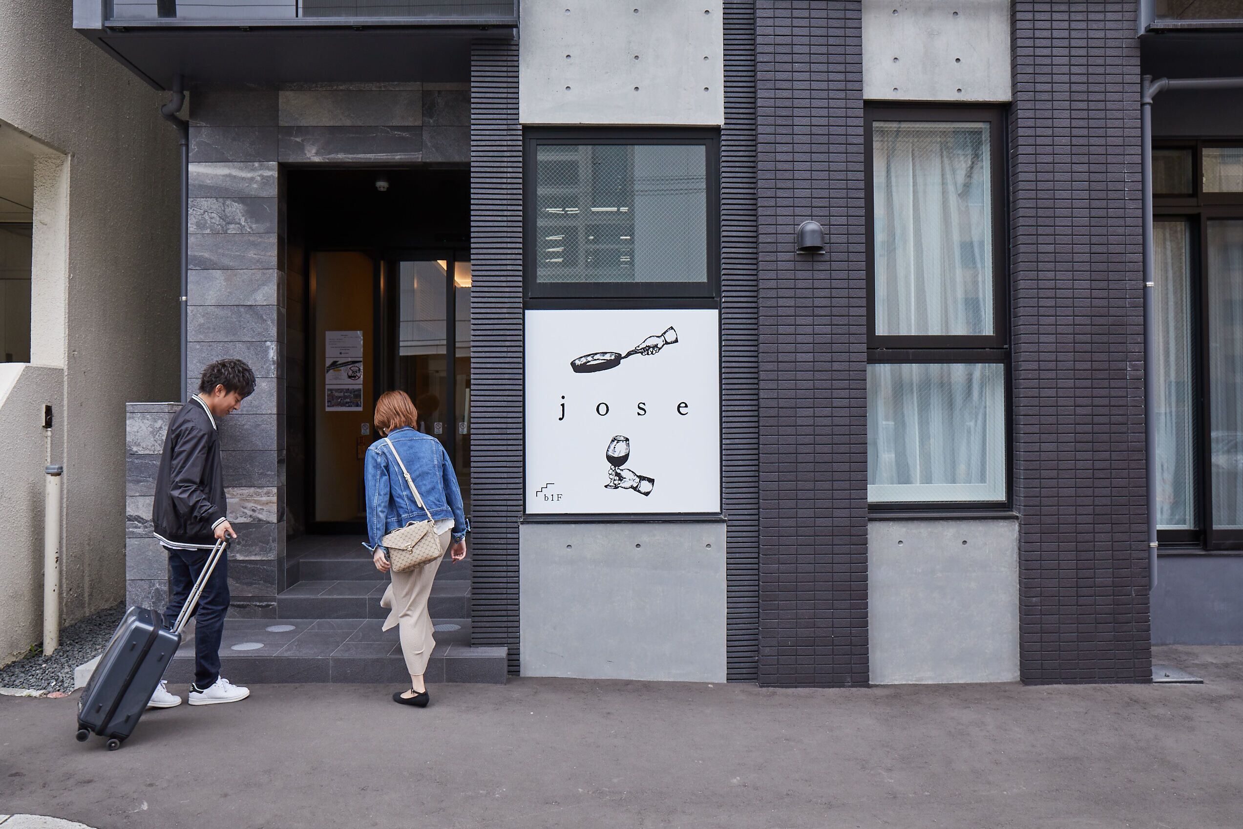 A building entrance with a sign reading "jose" and a person pulling a suitcase.