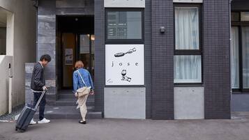 A building entrance with a sign reading "jose" and a person pulling a suitcase.