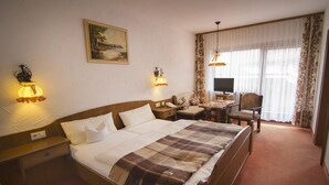 A hotel room with a large bed, a desk with a chair, a television, and two wall-mounted lamps. - Reikartz Hotel Bergpanorama Pfronten (Pfronten)
