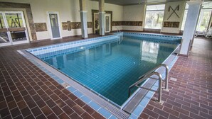 An indoor swimming pool with a tiled floor and walls, a metal ladder, and a door leading outside. - Reikartz Hotel Bergpanorama Pfronten (Pfronten)