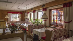A cozy restaurant with wooden walls, large windows with red curtains, and a variety of seating arrangements including booths and tables. - Reikartz Hotel Bergpanorama Pfronten (Pfronten)
