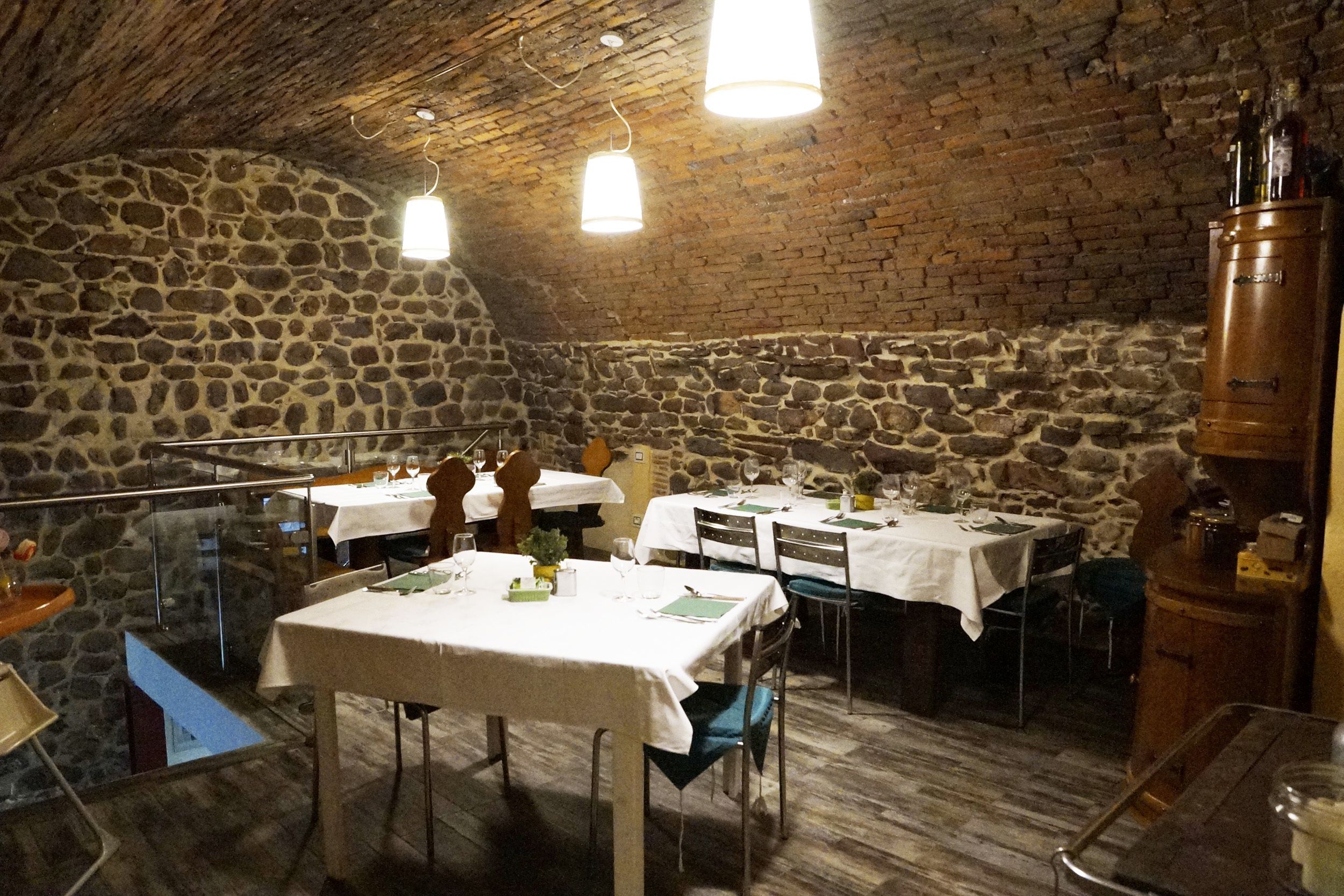 A restaurant with stone walls and wooden ceiling, featuring tables set for dining.