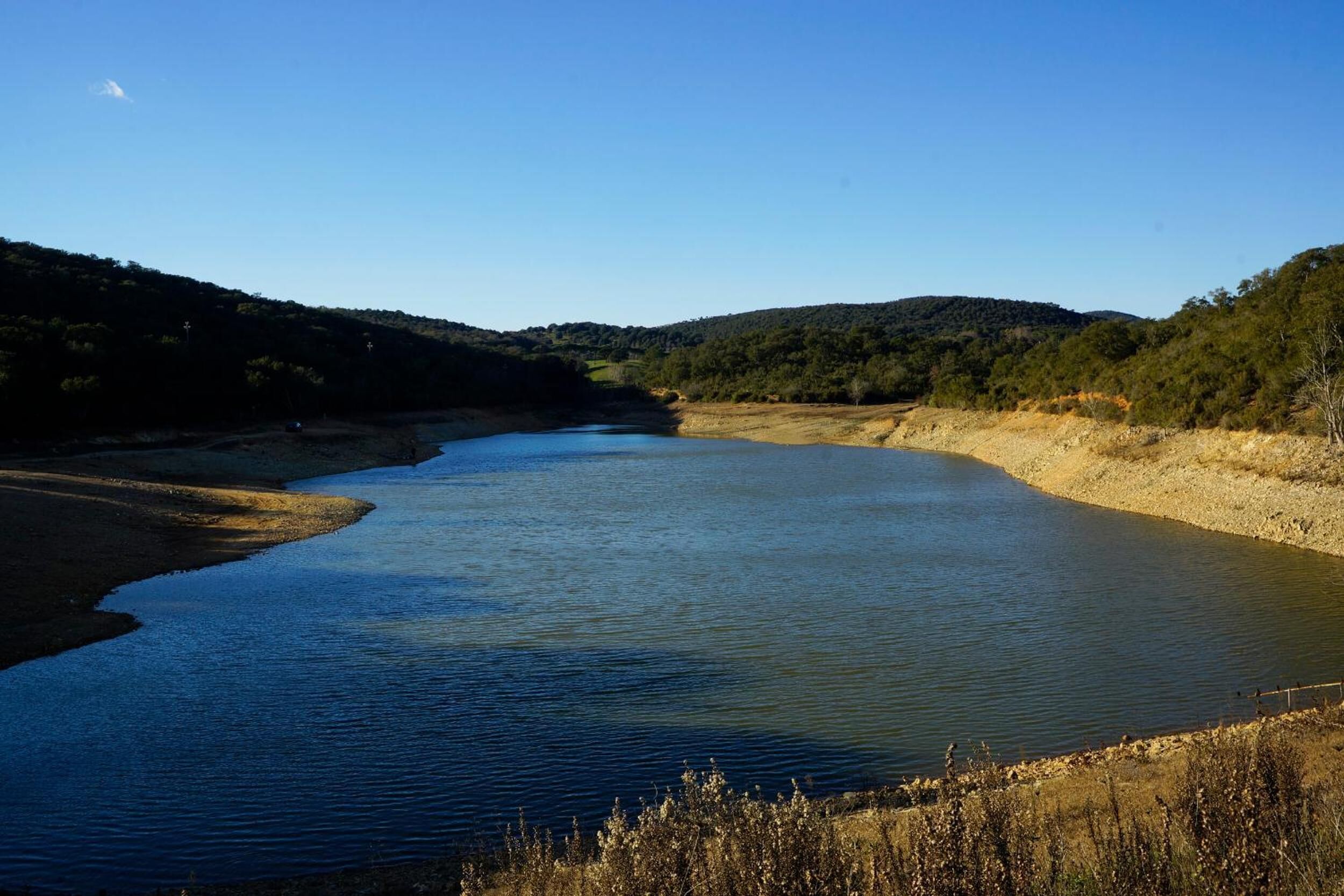 A river flowing through a hilly landscape with a clear sky.