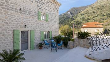 A stone building with a balcony, outdoor seating, and a view of a mountain.