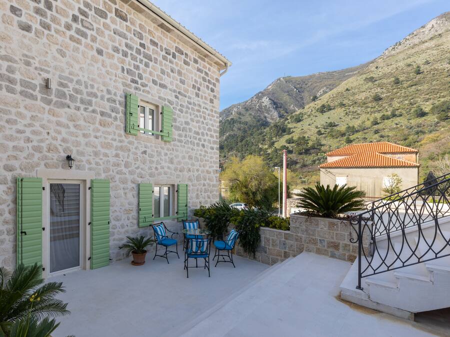 A stone building with a balcony, outdoor seating, and a view of a mountain.