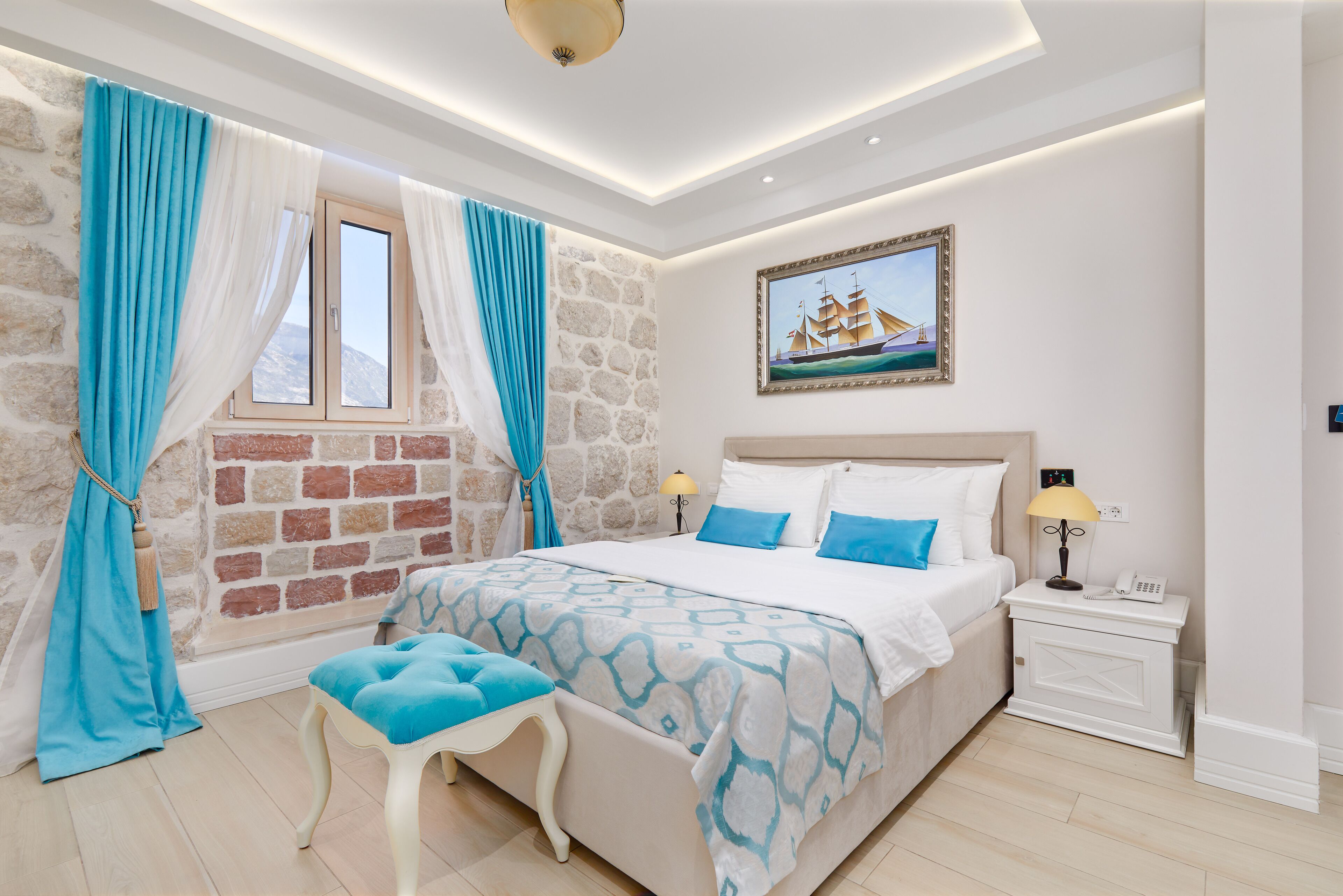 Ein Schlafzimmer mit Steinwand, einem Bett mit blau-weißer Bettwäsche, einem Nachttisch mit Lampe und einem Gemälde eines Schiffes an der Wand.