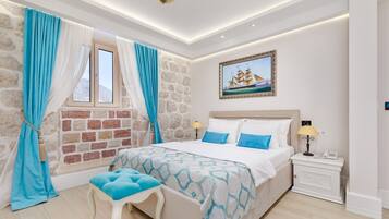 Ein Schlafzimmer mit Steinwand, einem Bett mit blau-weißer Bettwäsche, einem Nachttisch mit Lampe und einem Gemälde eines Schiffes an der Wand.