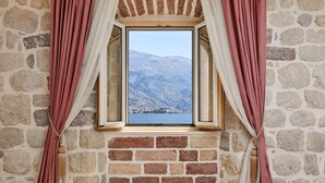 A room with a stone wall, a window with curtains, and a view of mountains.