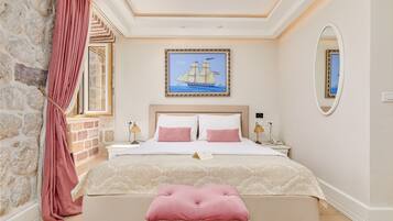 A bedroom with a large bed, a nightstand, a bedside table, a mirror, and a painting of a sailboat.