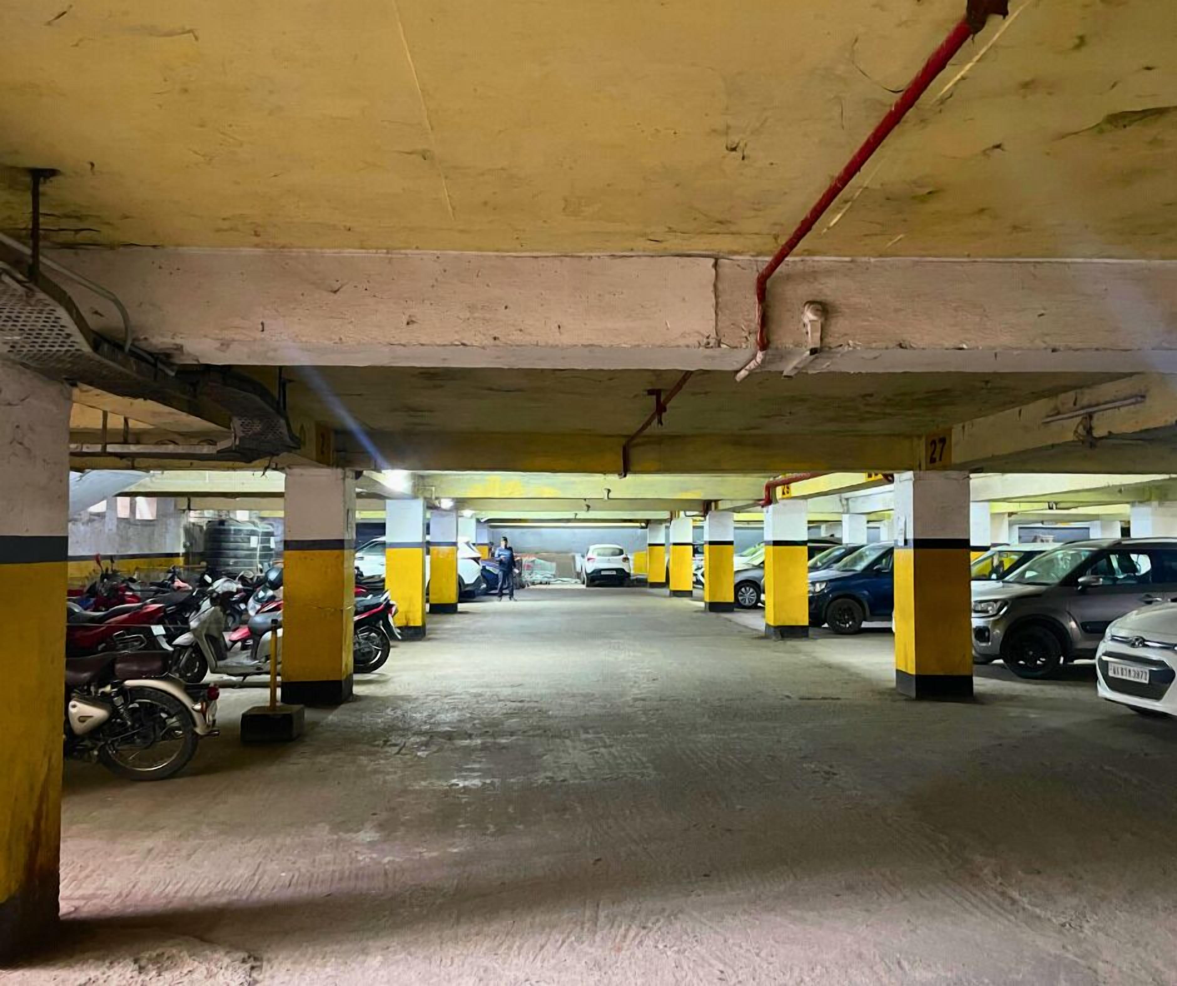 An underground parking garage with yellow and black pillars, concrete floors, and several parked vehicles including cars and motorcycles.