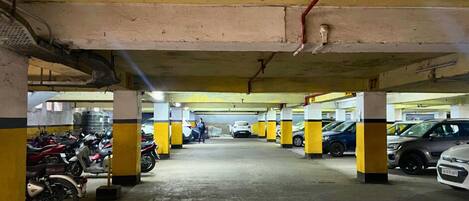 An underground parking garage with yellow and black pillars, concrete floors, and several parked vehicles including cars and motorcycles.