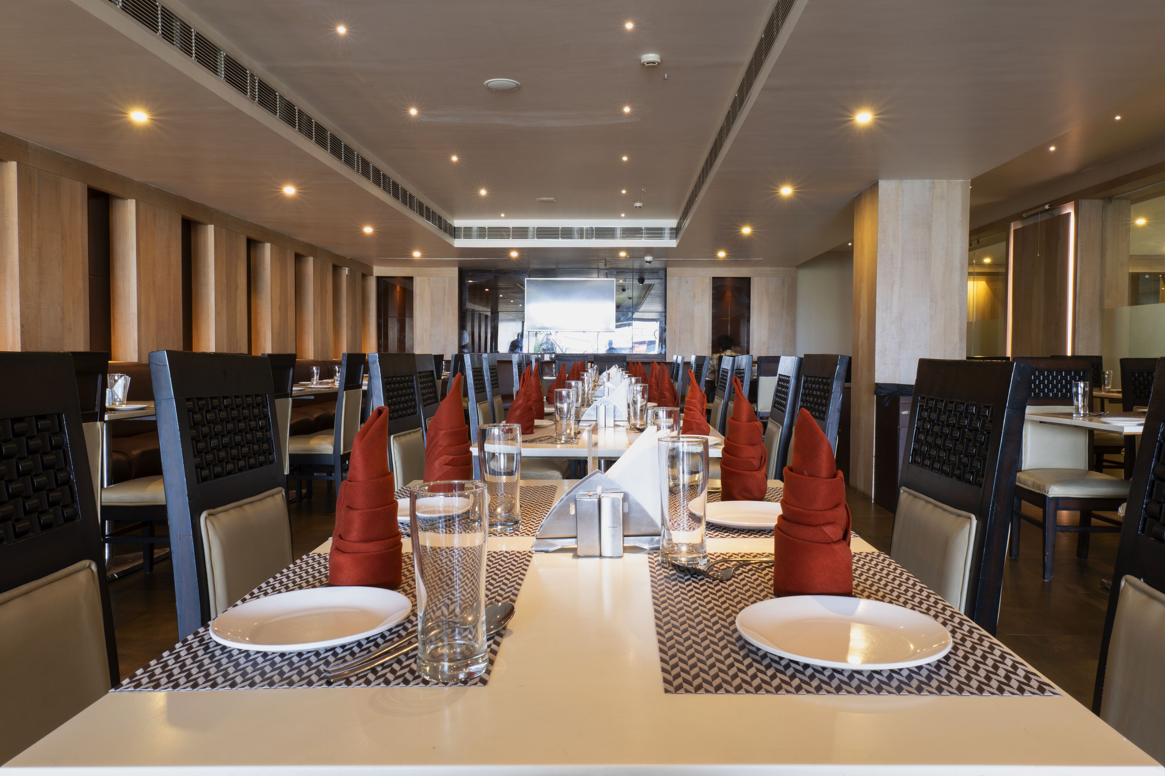 Un comedor moderno con mesas altas, sillas y una pantalla de proyección central.