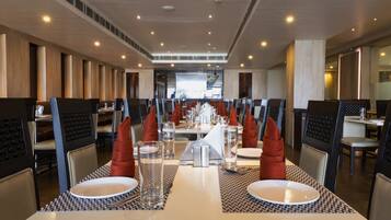 Un comedor moderno con mesas altas, sillas y una pantalla de proyección central.