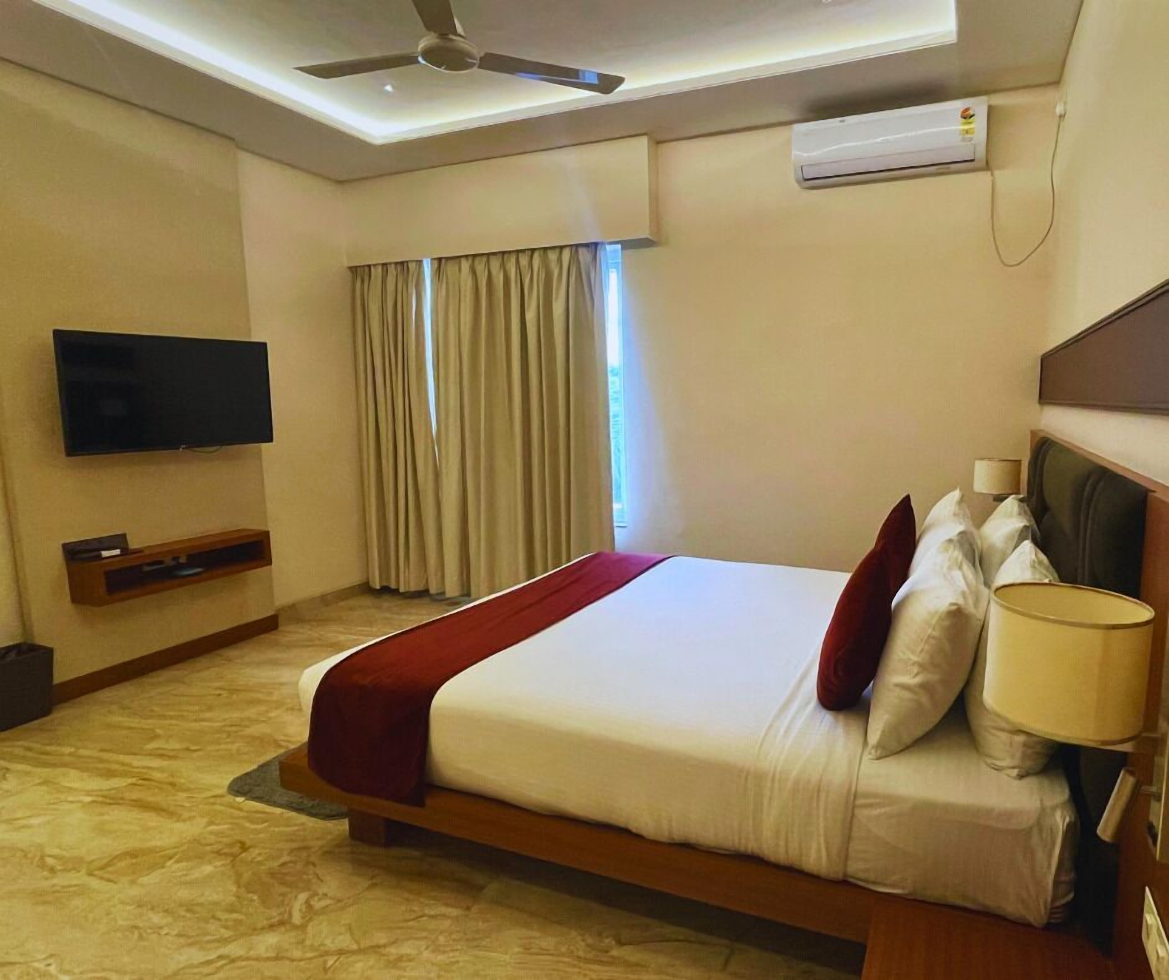 Habitación de hotel con cama, televisión, aire acondicionado y ventilador de techo.