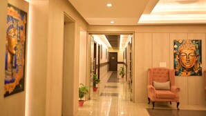 Pasillo de hotel con un muro espejado, un cuadro de Buda y un sillón rosa.
